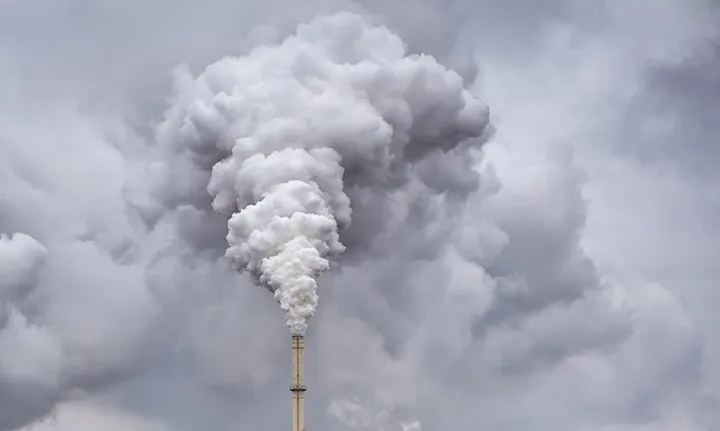 Smoke from factory pipe against dark overcast sky