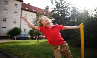 Little boy of 8-9 years turns around a support in the yard at the house.